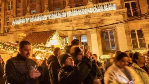 People celebrate Christmas in Birmingham city centre. The message "Merry Christmas Birmingham" is written in lights on the front of the council headquarters.