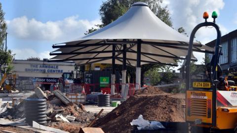 Shipley's market square with a new white canopy in the middle of the image surrounded by contractors' vehicles, rubble and piles of soil