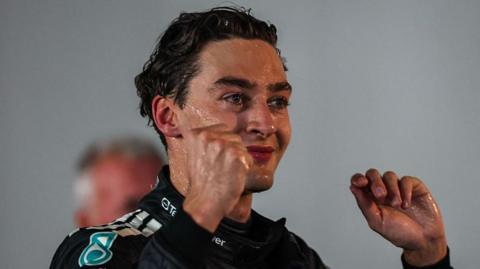A champagne-covered George Russell lifts his arms in celebration after winning the Singapore Grand Prix 