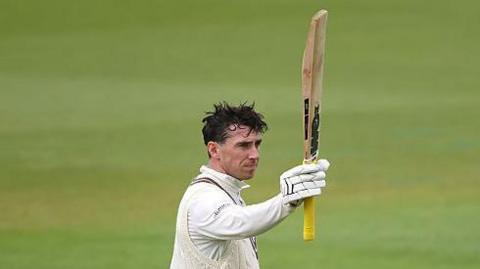 Dan Lawrence raises his bat after century