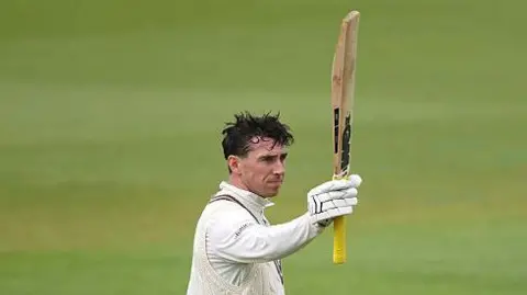 Dan Lawrence raises his bat after century