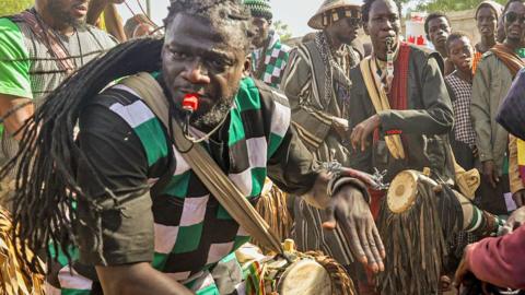 Baye Fall followers, some in colourful patchwork clothes, drumming and whistling on a street in Diourbel, Senegal