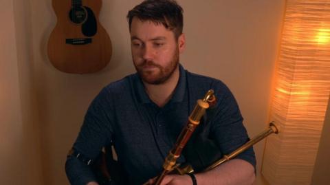 Chris McMullan in a blue shirt playing the uilleann pipes