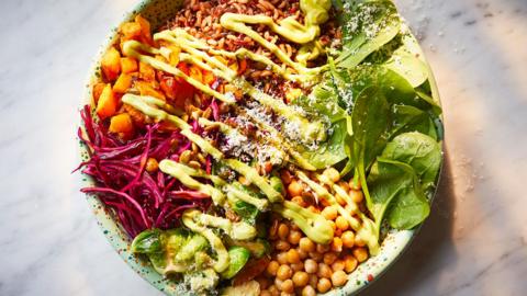 A bird's eye view of a bowl full of roast pumpkin, chickpeas, charred sprouts, red cabbage and topped with a creamy avocado sauce.