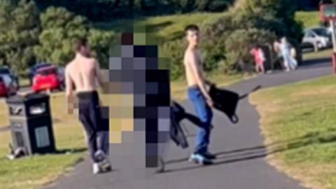 CCTV of three teens in a park, two are shirtless, the middle person is pixelated