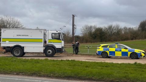 A picture of a bomb disposal lorry and police van outside a field, where the bomb was detonated.