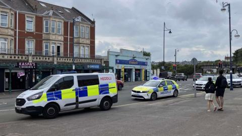 Police cars are parked along the street in front of Kaspas desserts and Greggs 