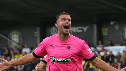 Innes Cameron with his arms outstretched, having scored for Barrow at Harrogate