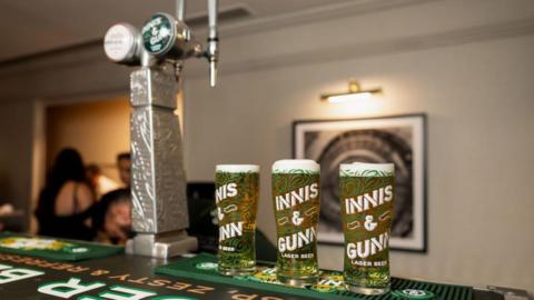 Three pints of Innis and Gunn on a bar with two Innis and Gunn taps next to it.