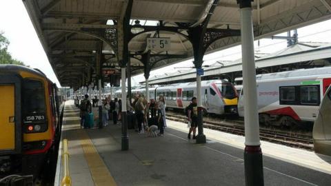 Two Greater Anglia trains at two platforms at Norwich railway station. People are milling about.