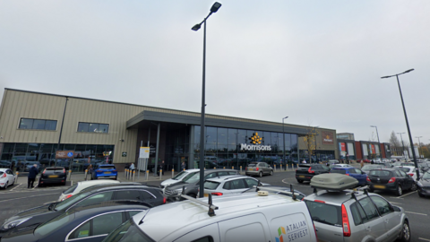 A general view of the Morrisons store in Kirkby, Merseyside. It is a glass-fronted building, including the Morrisons' logo, seen from the car park. 