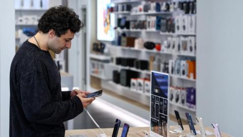 A man holds an Apple iPhone in a store that sells smartphones 