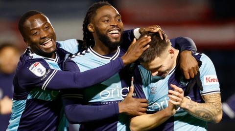 Aaron Morley receives congratulations from Wycombe Wanderers team-mates Fred Onyedinma and Daniel Udoh 