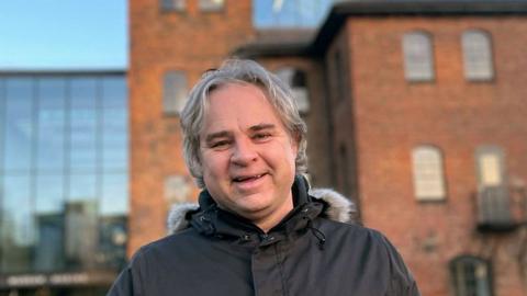 A man with grey hair and wearing a coat stood outside the museum of making in Derby city centre