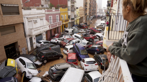 A woman looks out from her balcony at a pile-up of scores of cars in a flooded street in Valencia on 30 October