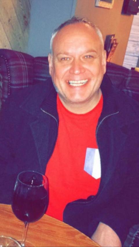 Smiling man with grey hair in red t-shirt and blue jacket sat on a sofa
