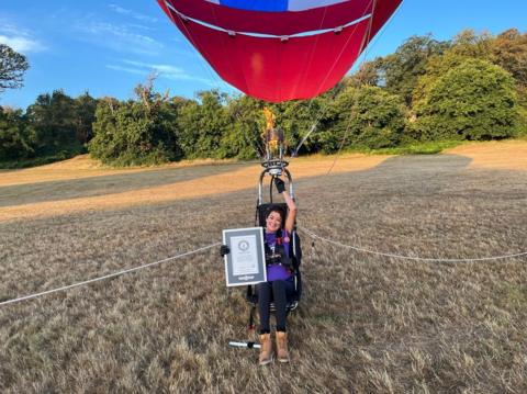 Woman in purple top sat in field with hot air balloon above