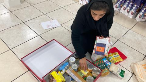 Trustee Gurdeep Kaur Sehra is kneeling on the floor of the temple and packing a christmas hamper.
