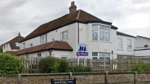 A white two-storey property with bay windows on both floors. There is a sign outside that reads "Flower Pots Day Nursery". 