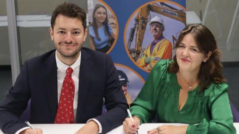 MP Jack Abbott and Julia Pike from Sizewell C smiling at the camera. Mr Abbott is wearing a dark suit with red tie. Ms Pike is wearing a dark green blouse.