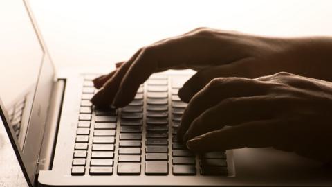 A close up of a laptop keyboard and a pair of hands typing keys.