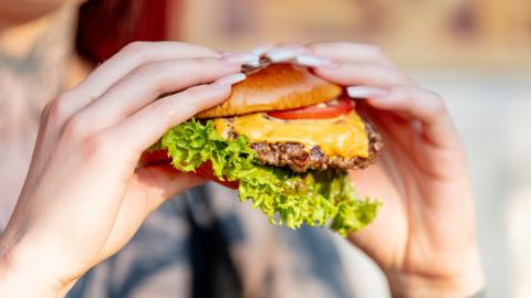 Woman holds freshly made cheeseburger outdoors in the summer sun. - stock photo