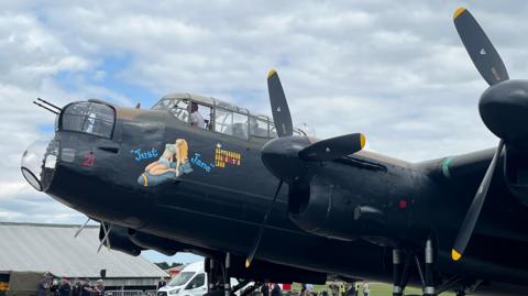 A side view of the nose of a black Lancaster Bomber with an image of a woman in a blue two-piece between blue writing reading "Just Jane".