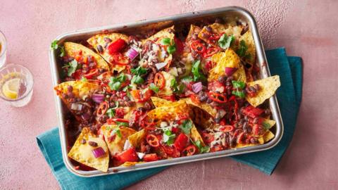 A metal tray filled with loaded nachos, covered in black beans, herbs and chillies.