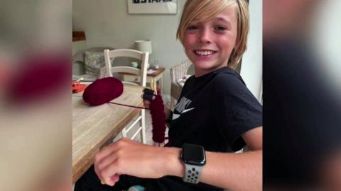 A young man is knitting at a kitchen table