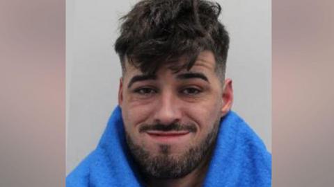 Custody image of Anthony Gilheaney, a man with short, dark, messy hair, facial hair, wearing a smirking expression.