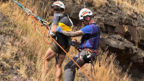 Two people wearing harnesses and helmets on a hillside