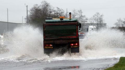 A lorry drives through a flooded road in County Antrim with spray coming up on either side of it