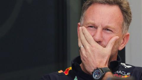 Christian Horner with his left hand over his mouth looking pensive.