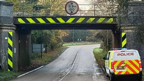 A bridge with a sign that reads 3.9m with a police van parked on the left. 