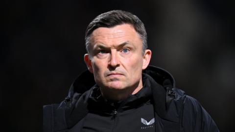 Paul Heckingbottom looks ahead with a furrowed brow and mouth set in a straight line. He wears a black rain jacket