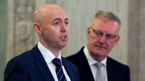 Ulster Unionist Party (UUP) leader Jon Burrows (left) and Mike Nesbitt MLA (right). Both men are wearing dark jackets and white shirts. Burrows is wearing a navy striped tie. He is balding. Nesbitt, who has glasses, is wearing a grey tie.
