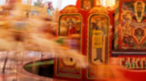 A blurred view of a merry-go-round at a funfair. The stand is on the right hand side, and horses are on the left. 