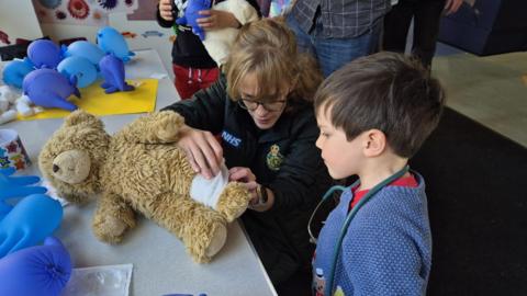 A teddy being bandaged up by a member of staff and a young boy