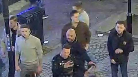 A blurry CCTV image taken from above of seven men in a high street.