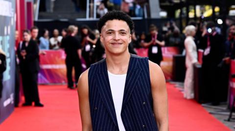 Actor Lee Braithwaite on the red carpet premiere of the new film, wearing a blue striped waistcoat and white vest. 