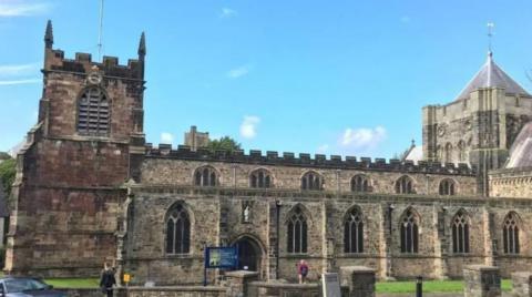 An exterior view of Bangor Cathedral, it is a clear day and there are two people in the foreground of the picture, one walking towards the front door of the cathedral.