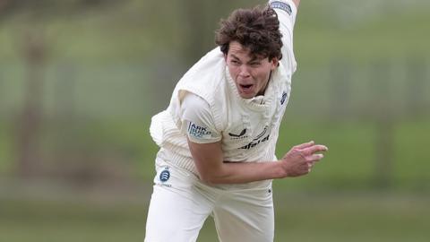 Henry Brookes crouched forward with his right arm held up in the air behind him after he bowls a ball during a friendly for Middlesex