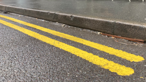 Close up of a double yellow lines on a road next to a curb. 