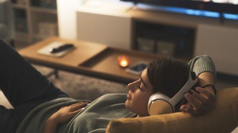 Young woman resting on the couch at home, she is wearing wireless headphones and listening to music - stock image