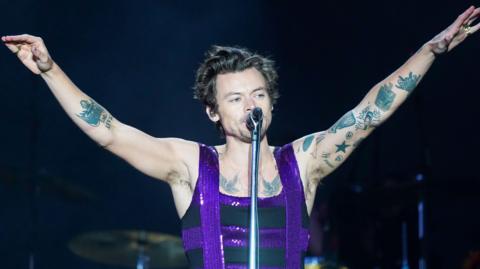 Harry Styles stands on stage at Radio 1's Big Weekend at the War Memorial Park in Coventry in 2022 wearing a black sleeveless top with purple sequin details