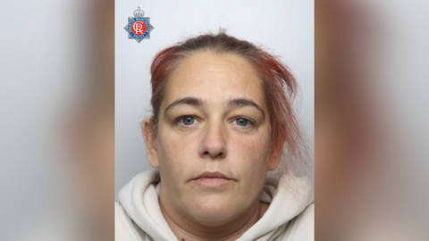 A woman with blue eyes and red dyed hair in police mugshot.
