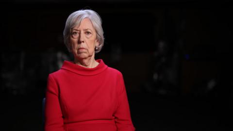 lady sitting in a dark room with red jumper for an interview 
