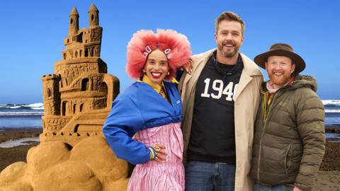 Sadie Clayton, Iain Stirling and Jamie Wardley standing in front of a sand sculpture