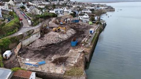 The abandoned slipway with rubble in the centre with a yellow digger working on the slipway.