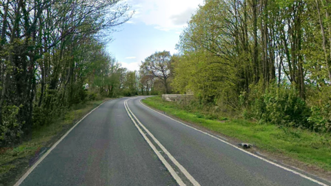 A stretch of the A40 through the Cotswolds as it goes around the bend, surrounded by trees.